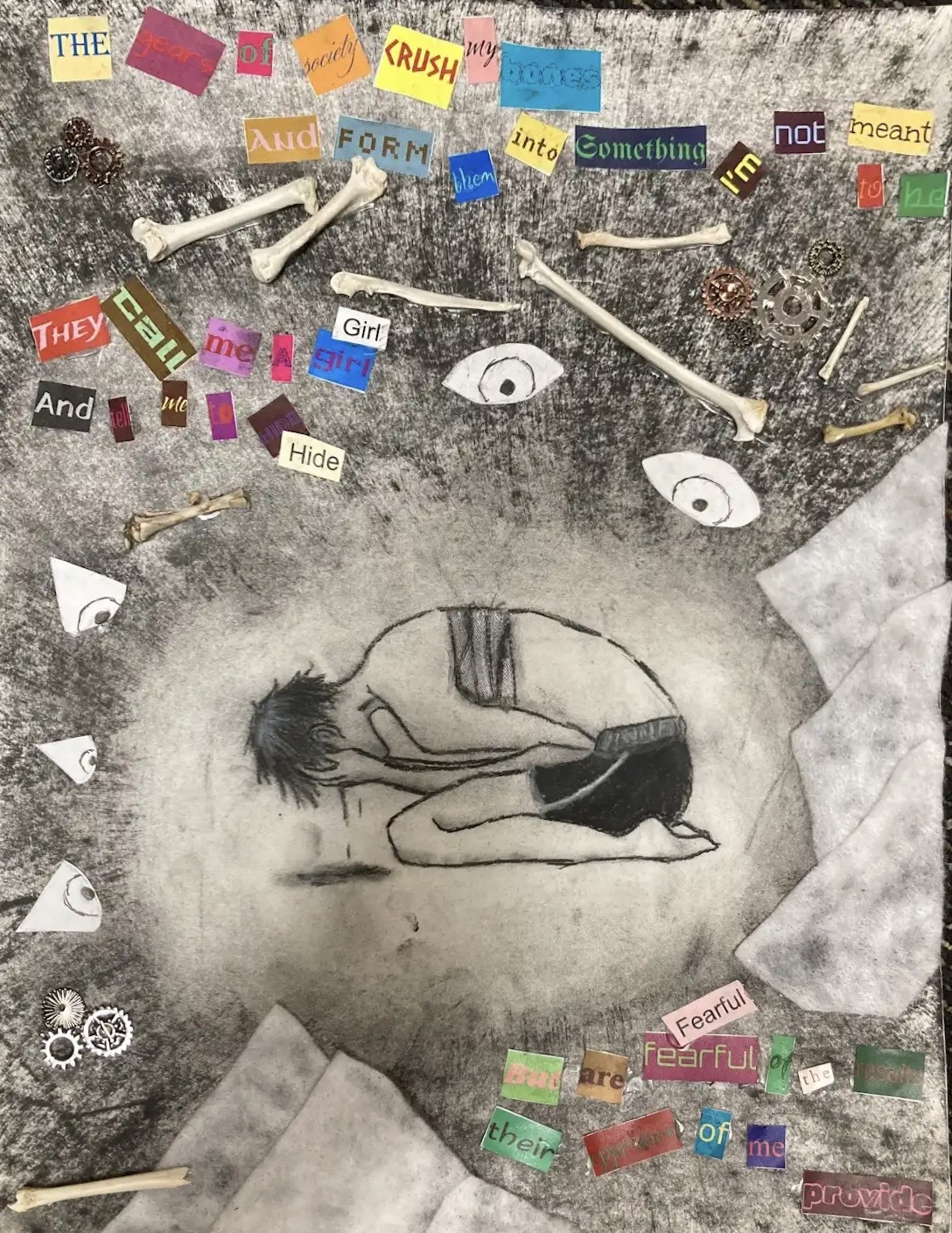 a collage-style charcoal drawing, depicting a masculine-presenting figure, in the middle of the page, hunched over on their knees and holding their head in their hands. They are wearing nothing but black shorts and binding bandages around their chest and back. Tears are falling from their covered face and onto a puddle on the ground. Everything is drawn in black, white and grey tones.
Surrounding them are paper eyes, small bones and metal cogs.
There is writing above and below the figure, with each word cut out from a different magazine or newspaper, therefore giving them all a different colour and font. Some of the words have been repeated.
The writing reads: “The gears of society crush my bones and form them into something I’m not meant to be. They call me a girl (girl) and tell me to hide (hide) but are fearful (fearful) of the results, their [unintelligible] of me provided.”
